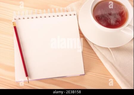 mock up image notebook with blank white page with red pen on wooden table and hot cup of tea. Notepad on a wooden table. copy space. Stock Photo