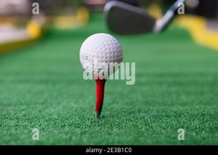 Green artificial grass golf field, white ball standing on red tee peg and iron driver stick club on background prepare to strike Stock Photo