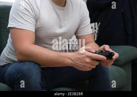 Unrecognizable young man playing video games with a gamepad sitting on sofa. Gamer at home. Stock Photo
