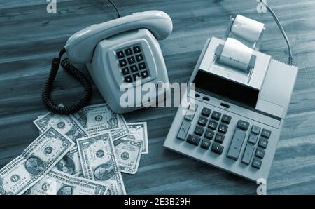 Old fashioned calculator, telephone and dollars on desk Stock Photo