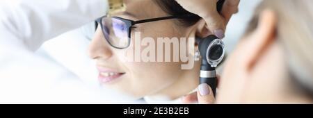 Otolaryngologist doctor examining patients ear with otoscope in clinic Stock Photo