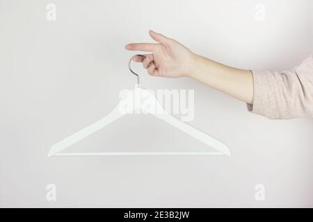 White wooden hanger in female hands against the light wall. Store concept, sale, design, empty hangers. Black friday. Spring autumn outfit. Minimal co Stock Photo