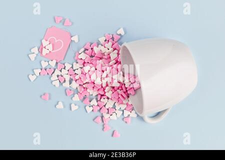 White and pink sugar hearts spilling out of white tea cup on pastel blue background Stock Photo