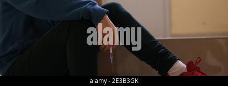 Addict sits with his head down and holds syringe in his hands. Stock Photo