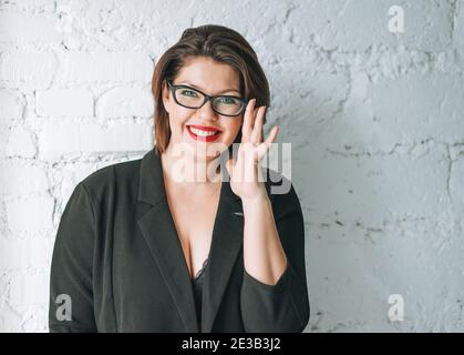 Beautiful smiling young woman business lady in glasses and black jacket against white wall Stock Photo