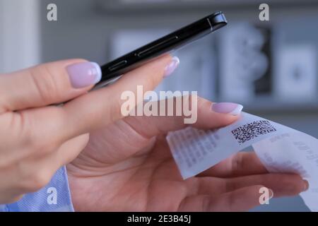 Woman using smartphone and scanning qr code on cash shop receipt paper - closeup Stock Photo