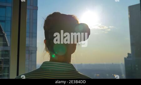 VR concept - young woman using virtual reality headset against skyscraper window Stock Photo