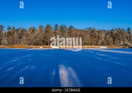 Frozen Lake Cover in White Snow with Long Blue Shadows from Trees Stock Photo