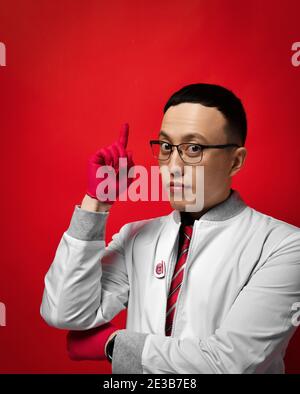 Portrait of young man doctor urologist or proctologist in medical gown and latex gloves holds forefinger up gesturing Stock Photo
