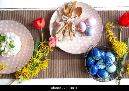 Plates with Easter cake, flowers and Easter eggs. Table setting for the Easter holiday. Stock Photo