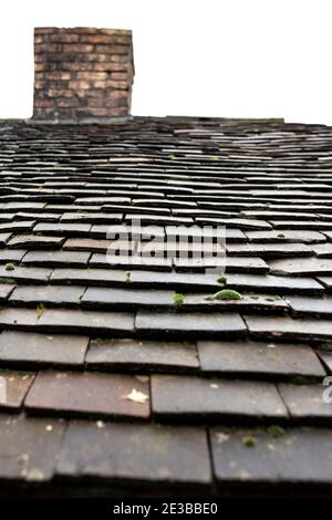 Old weathered clay roof tiles on a house with chimney.  White background Stock Photo