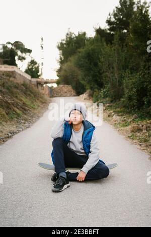 Portrait Of A Teen Boy sitting on his skateboard in a path Stock Photo