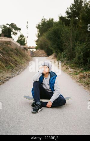 Portrait Of A Teen Boy sitting on his skateboard in a path Stock Photo