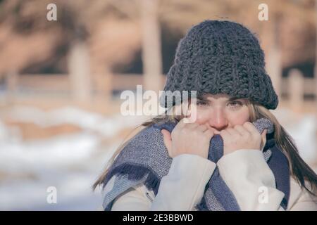 Winter horizontal portrait of smiling beautiful blonde girl in a snow day with a gray hat and long scarf. Closeup beauty photo of winter outdoor 2021. Stock Photo