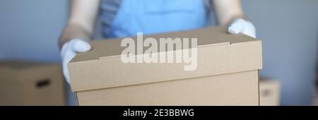 Man in overalls and gloves hold large cardboard box in his hand close-up. Stock Photo