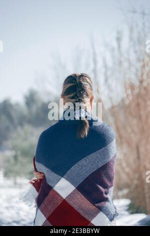 Detail of the girl's back with her hair collected in a braid looking and appreciating the snowy landscape with a with a scarf around her body-Winter Stock Photo