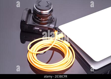 Digital photo camera connected to laptop with orange rolled cable. Stock Photo