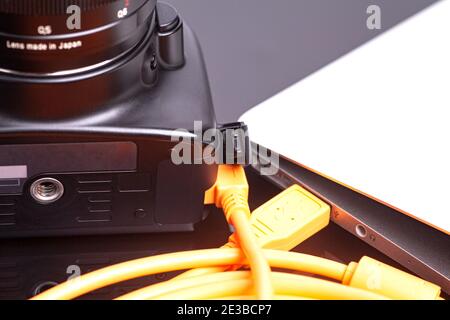 Digital photo camera connected to laptop with orange rolled cable. Stock Photo