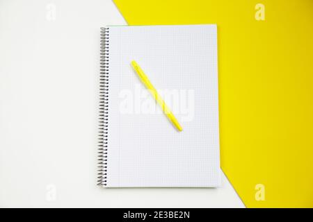 Top view of an open notebook and a pen against white and yellow background Stock Photo