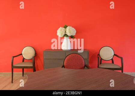 Contemporary Minimalist Dining Room with Dining Table & Modern Dining Chairs Photographed Against a Red Wall Stock Photo