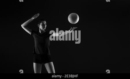 Volleyball girl hold and kick ball on dark background. Player doing sport workout online. Sport and recreation concept. Black and white color filter Stock Photo