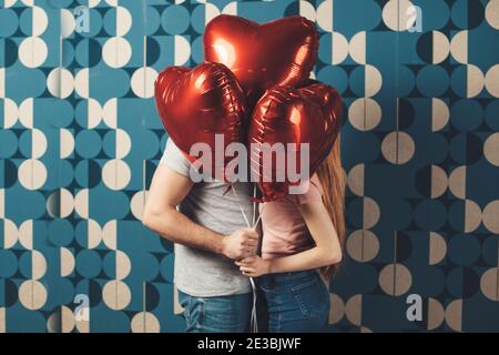Caucasian couple kissing behind the balloons on a blue wall celebrating valentines day Stock Photo