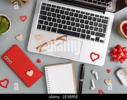 Red Mobile phone, notebook, glasses and valentines day decorations near laptop top view on grey table Stock Photo