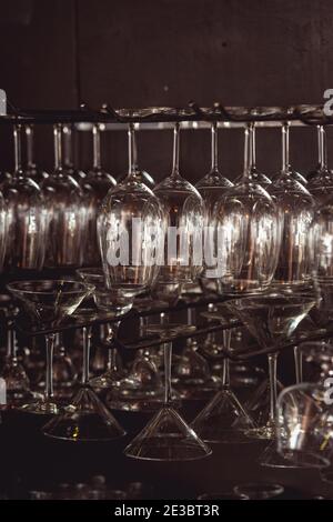 raws of glasses for a margarita, martini, grog and liqueur hanging upside down in bar at arestaurant, dark background Stock Photo