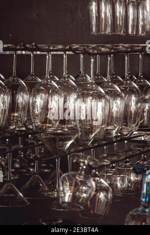 raws of glasses for a margarita, martini, grog and liqueur hanging upside down in bar at arestaurant, dark background Stock Photo