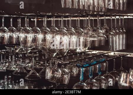 raws of glasses for a margarita, martini, grog and liqueur hanging upside down in bar at arestaurant, dark background Stock Photo