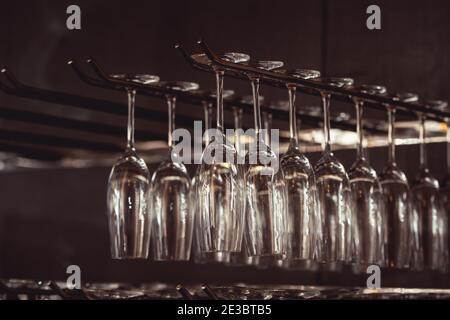 raws of glasses for a margarita, martini, grog and liqueur hanging upside down in bar at arestaurant, dark background. Stock Photo