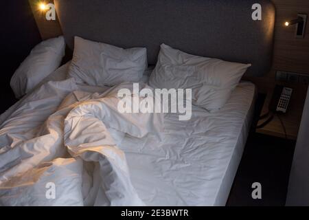 Unmade empty bed in an hotel room. Low light Stock Photo