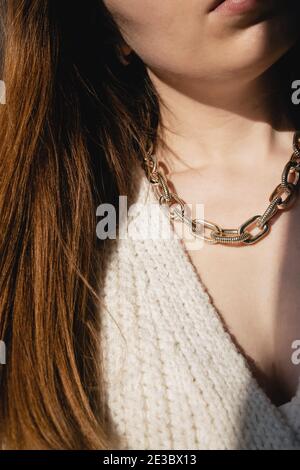 Close-up young woman in white sweater wearing golden chain necklace. Stock Photo