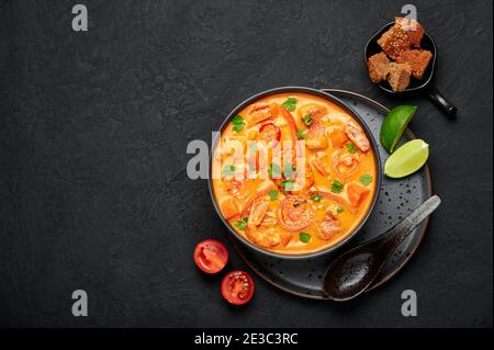 Moqueca with Fish and Shrimps in black bowl on dark slate table top. Brazilian sea food curry dish with coconut milk and vegetables. Top view. Copy sp Stock Photo