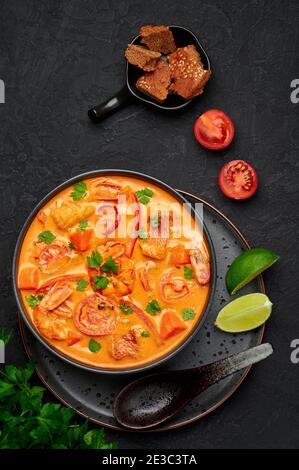 Moqueca with Fish and Shrimps in black bowl on dark slate table top. Brazilian sea food curry dish with coconut milk and vegetables. Top view Stock Photo