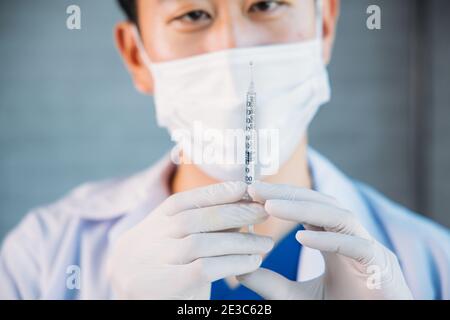 Close up of male Asian doctor holding a vaccine injection needle ready for vaccination. Young lab technician scientist at work Stock Photo