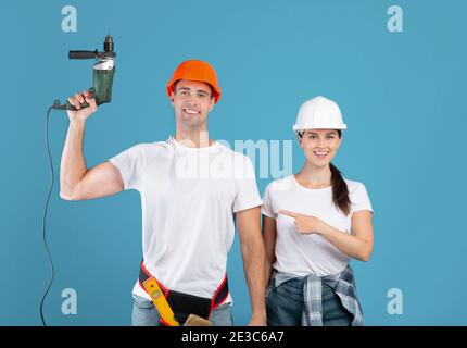 Repair Services. Happy Millennial Woman Pointing At Man With Drill In Hands Stock Photo