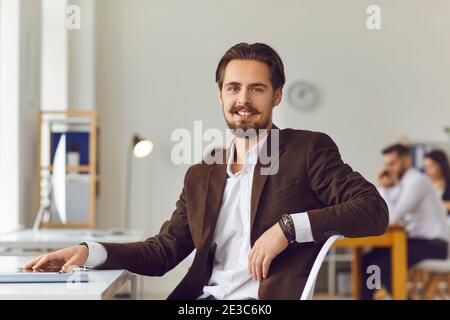 Handsome young business leader sitting at desk in office smiling and looking at camera Stock Photo