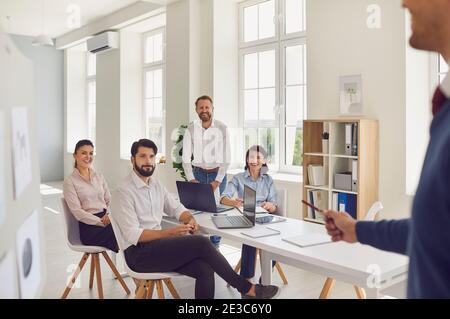 Young man discussing something while his colleagues listen to him sitting at an office desk. Stock Photo