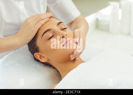 Positive relaxed woman getting procedure of facial massage from cosmetologists hands Stock Photo