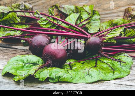 Beetroot tubers with green leaves on wooden table. Preparation of fresh salad. Fresh vegetables for vegetarian cooking. Beets on street market stall. Stock Photo