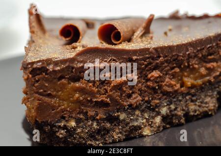 Digestive biscuit base with chocolate cheesecake and pockets of salted caramel sauce, topped with chocolate ganache, milk chocolate curls, and gold sh Stock Photo