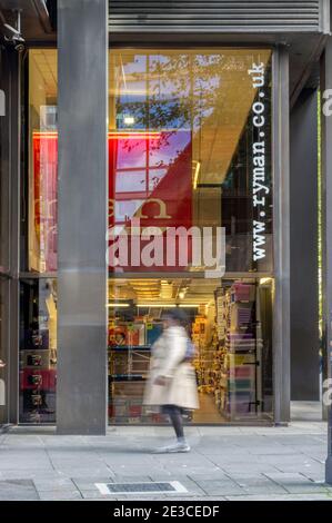 Woman (motion blurred) walking in front of a branch of Ryman, stationers. Stock Photo