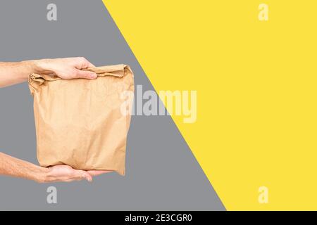 Close up female holds in hand brown clear empty blank craft paper bag for takeaway Delivery service concept. Copy space. Trendy colors 2021 - Gray and Stock Photo