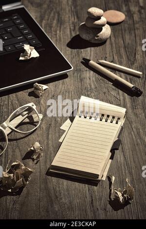 Creative writing, story-boarding, writer's block. Concept still life, arrangement on wooden table. Open blank paper pad. Crumpled paper pages. Laptop Stock Photo