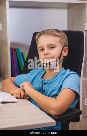 Home learning, online education. Schoolboy with glasses studies at home. Boy while sitting at table in front of laptop and looks at camera. Stock Photo