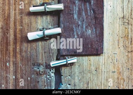 Three small rolls of white papers notification inserted into old rusty padlock hasp on the old wooden door. Bulletin sticking out at the gate of the a Stock Photo