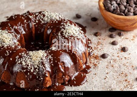 Chocolate cake with melted  pudding icing and chocolate chips in a bowl in the background. The decoration of this delicious cake was finished with spr Stock Photo