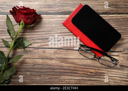 Flat lay view of a red notebook, red rose, smartphone, pen on a wooden background. Top view of modern office workplace. Stock Photo