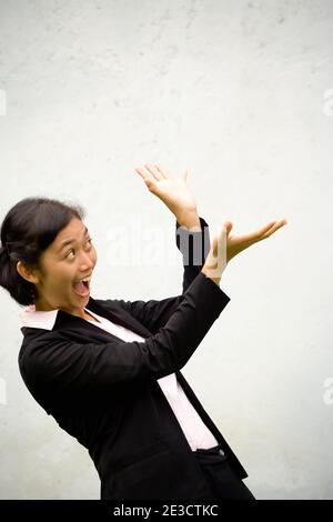 Pretty Asian businesswoman seems to be surprised going to catch something (can be a reward, bonus, prize, etc.) that is going to fall on her. Stock Photo